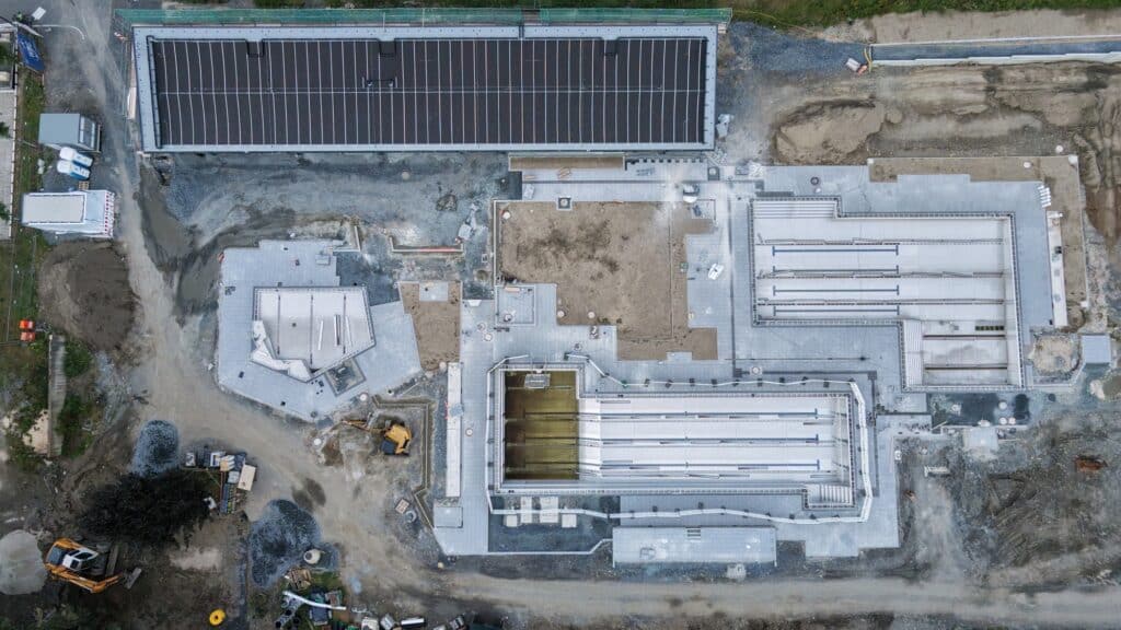 Eine Baustelle aus der Luft fotografiert. Man erkennt zwei große Schwimmbecken und das Dach eines Gebäudes mit Solarplatten.