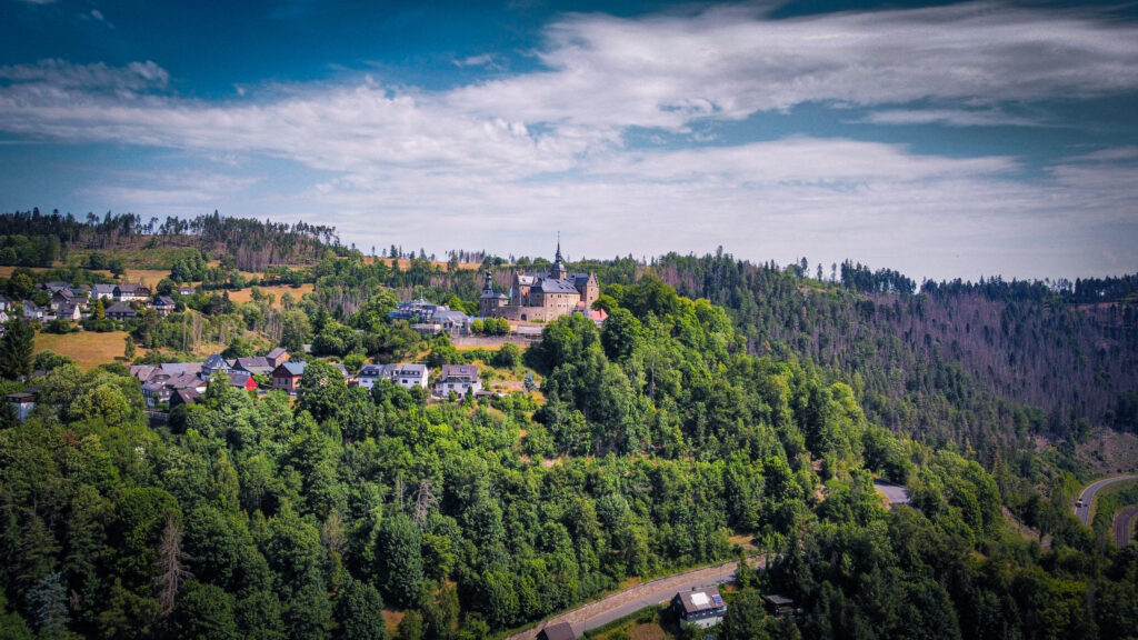 Ein Dorf, das entlang eines Mittelgebirgshügels liegt. Es ist rundherum sehr grün